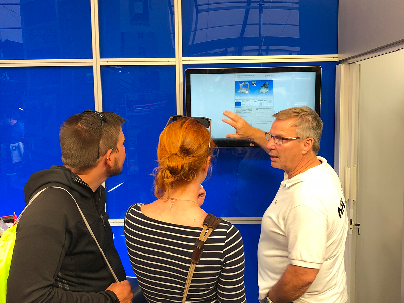 Außendienstmitarbeiter zeigt Besucherpaar Produkte von Elspro am Monitor